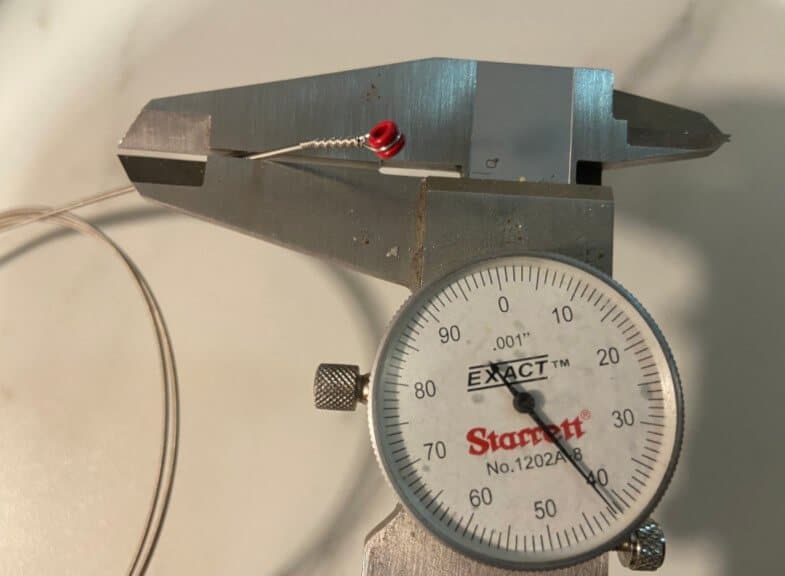 Measuring a guitar string with a caliper tool.